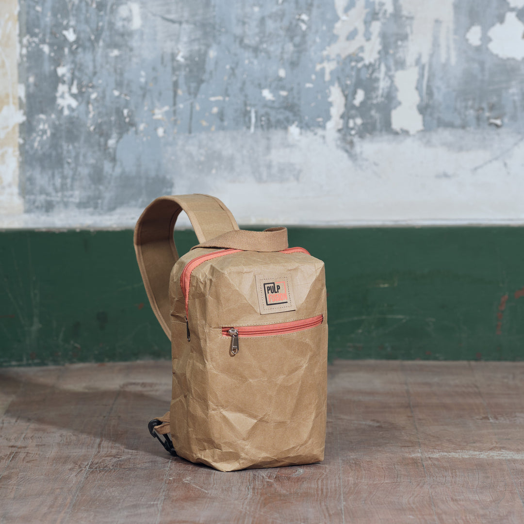 Brown leather bag with pink zipper on a wooden floor against a wall with peeling paint.